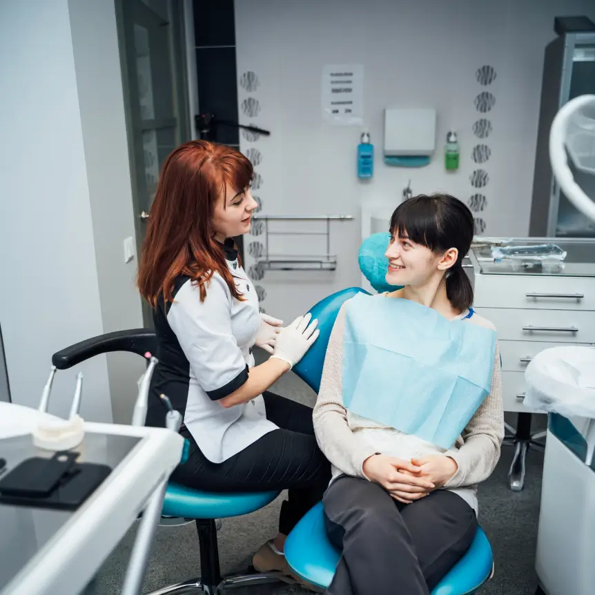 A dentist consults with a smiling patient seated in a dental chair. The setting is a modern clinic, conveying a sense of professionalism and care.