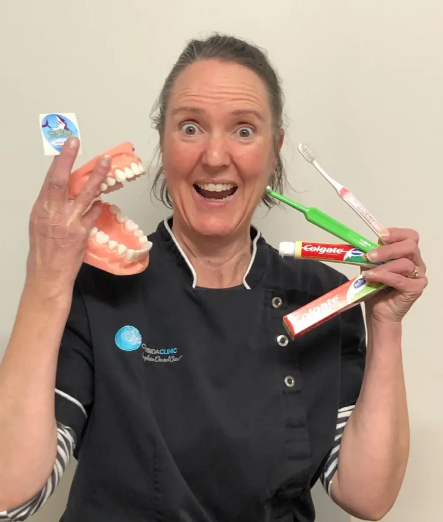 Dr Snell wearing black dental uniform enthusiastically holds dental model, toothbrushes, and toothpaste, conveying excitement and dental care awareness.