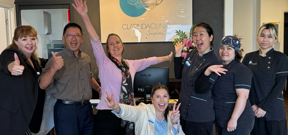 Clarinda Staff smiling giving thumbs up and peace signs in a warmly lit clinic reception.