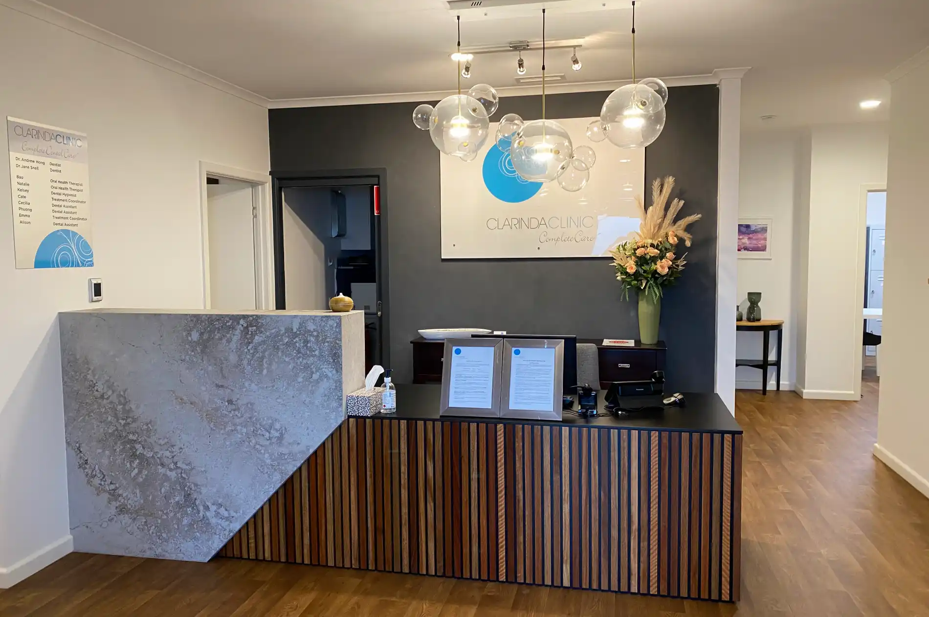 Modern Clarinda Clinic reception with a wooden counter, decorative vase with flowers, and bubble lights.
